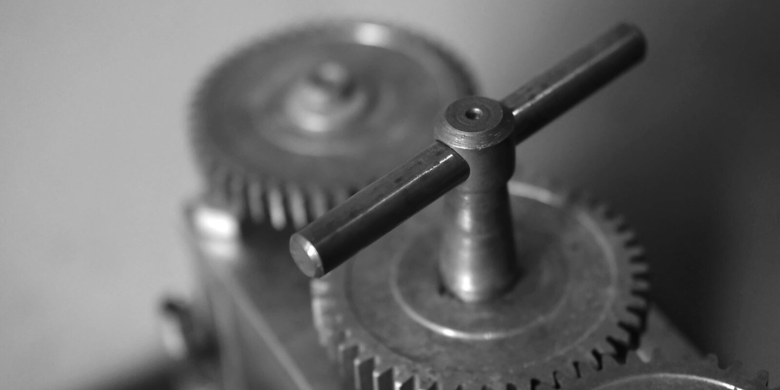 Närbild i svartvitt av metallkugghjul och vevhandtag i en mekanisk apparat med suddig bakgrund