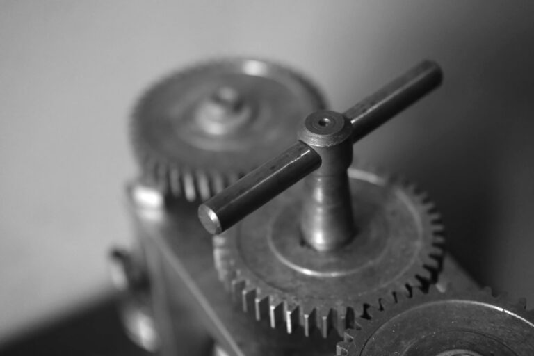 Närbild i svartvitt av metallkugghjul och vevhandtag i en mekanisk apparat med suddig bakgrund