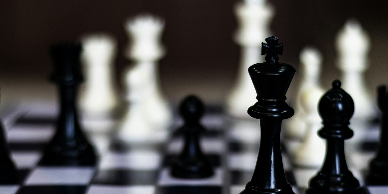 Närbild på svart schackkung och löpare på schackbräde med suddiga vita pjäser i bakgrunden