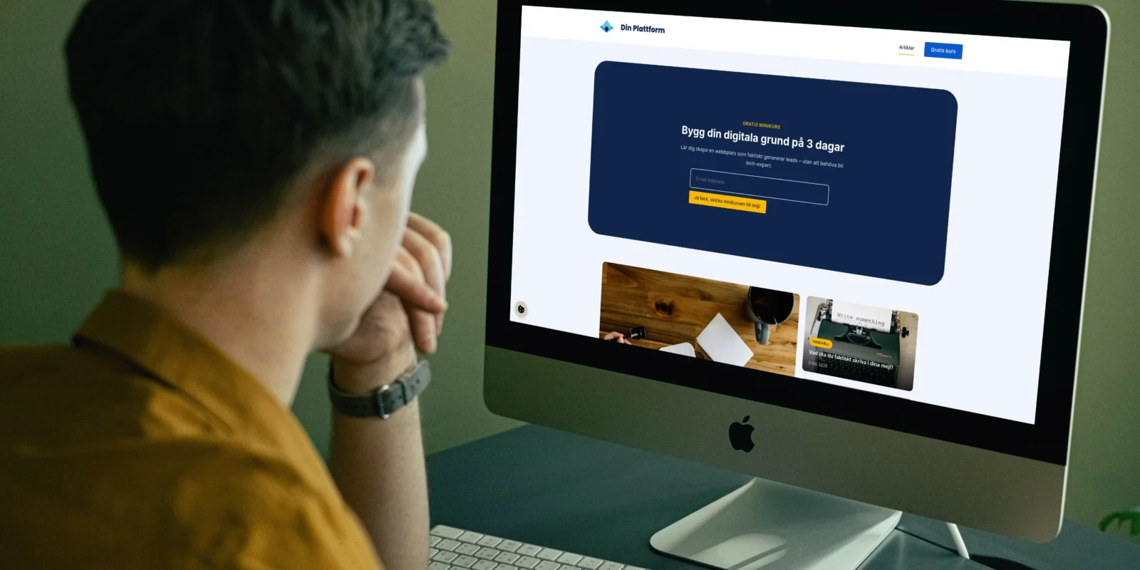 Man som arbetar vid skrivbord och tittar på en iMac med webbplats för digital kurs öppen på skärmen