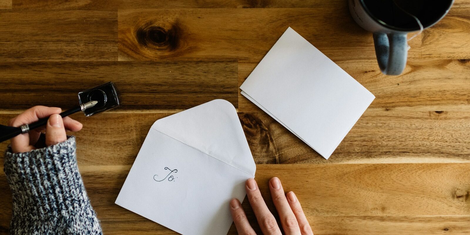 a person writing on a piece of paper next to a cup of coffee